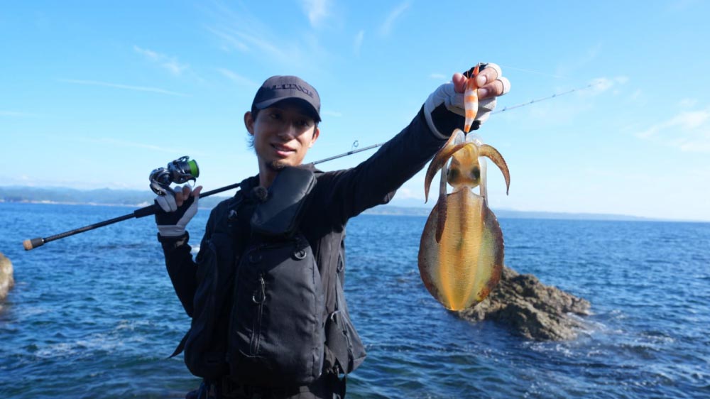 釣り上げたイカがかかったままのエギを左手で持って掲げ、笑顔を見せる黒神
