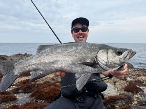 釣り上げた魚を両手に持って掲げ、満面の笑みを見せる男性