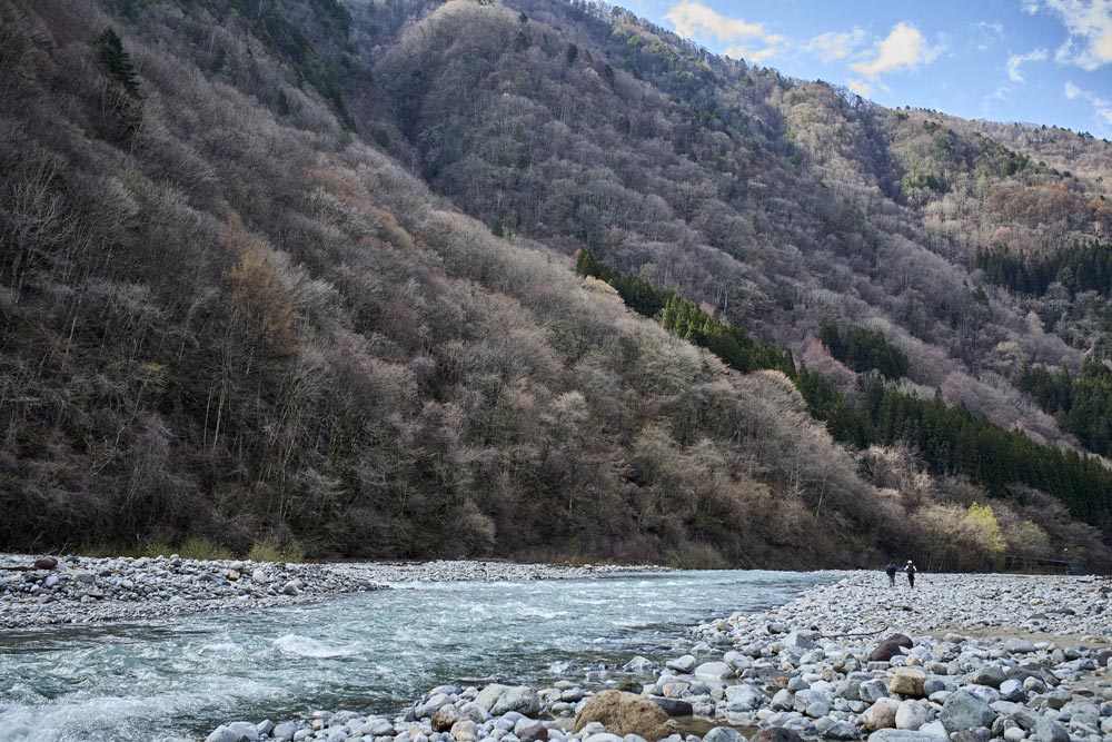 山に囲まれ開けた瀬と、遠方の河岸を歩く長谷川とスタッフ