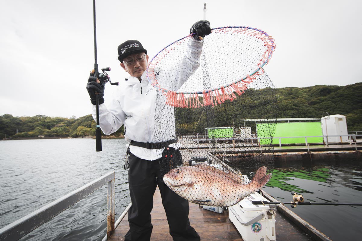 右手に竿、左手にタモ網に収まった真鯛を持つ男性
