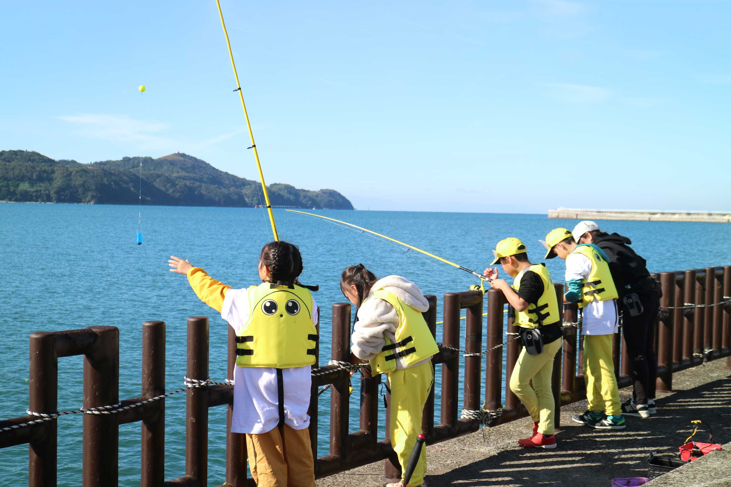 堤防を背に、釣った魚を持ち笑顔を見せる家族