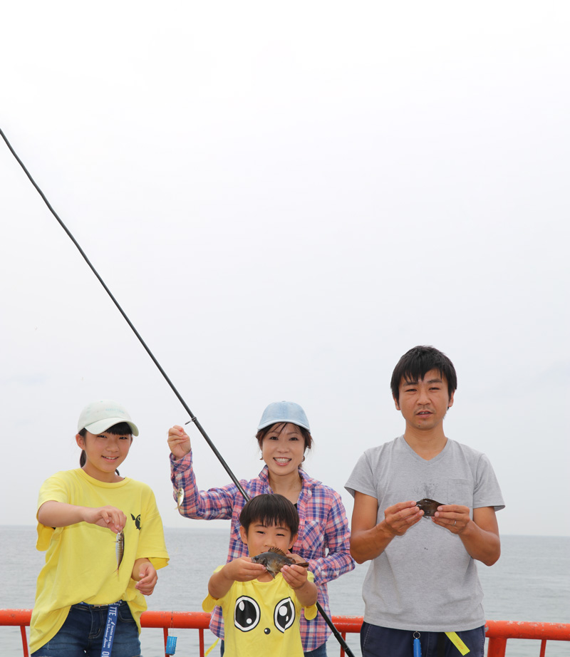 堤防を背に、釣った魚を持ち笑顔を見せる家族