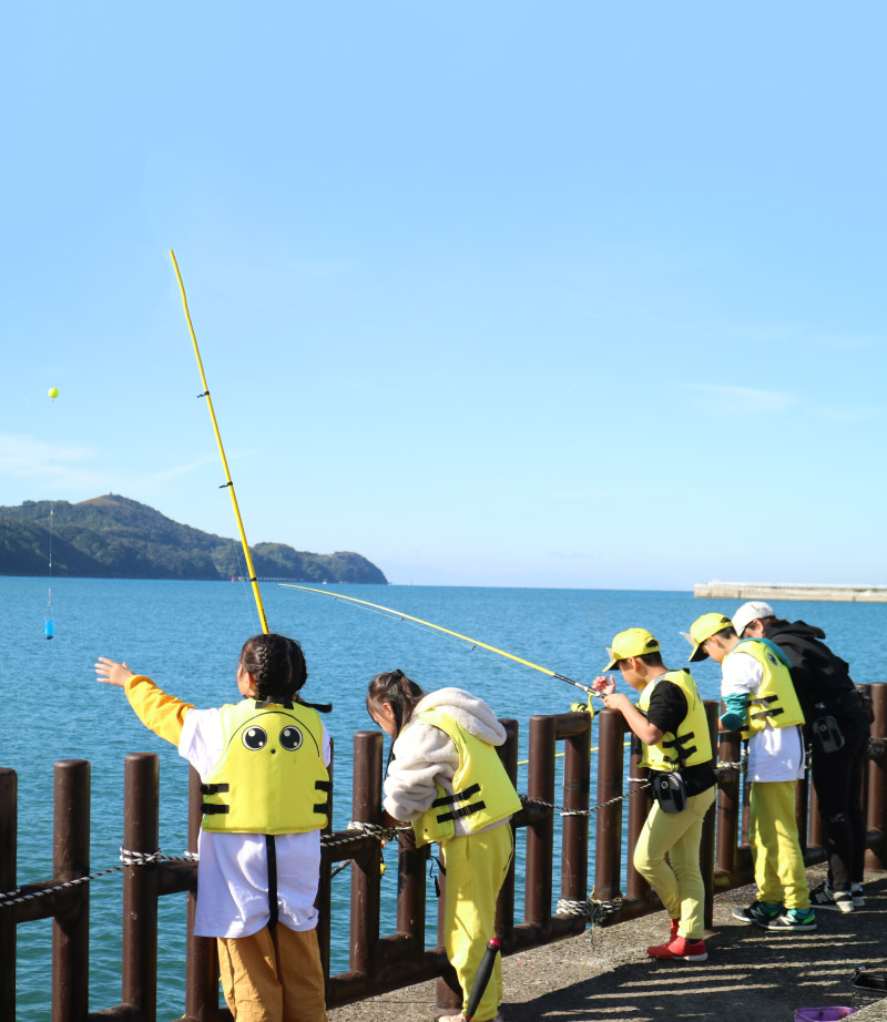 堤防を背に、釣った魚を持ち笑顔を見せる家族