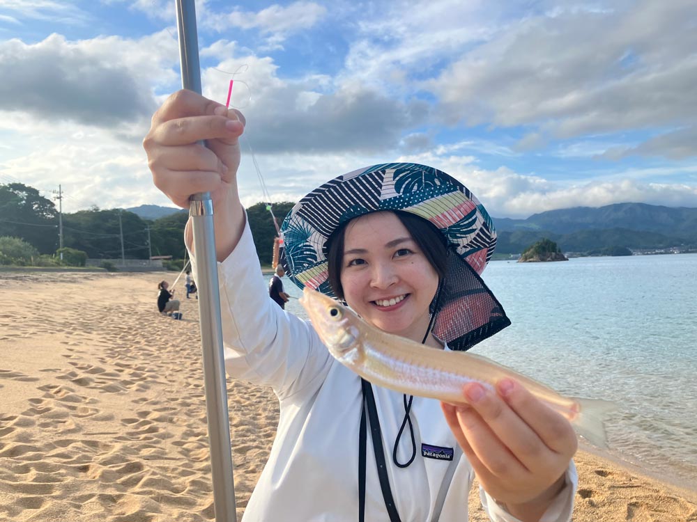 砂浜で釣れた魚を手に笑顔の女性