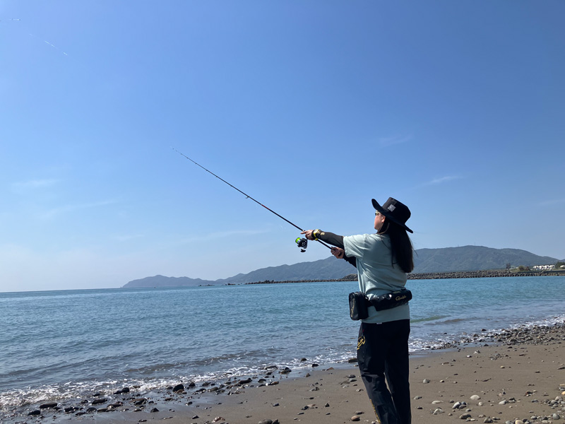 砂浜で竿を振り、仕掛けを海へ投げる女性